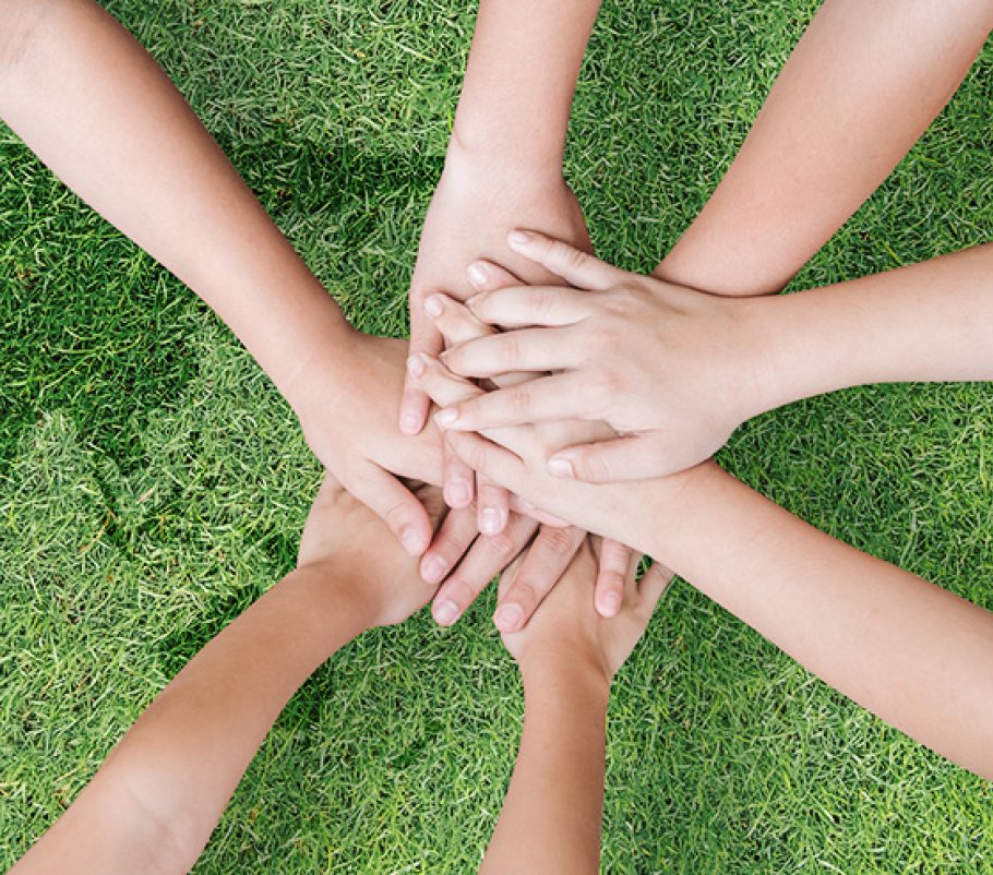A pile of hands laying on a lawn with an embedded shape of a world map.